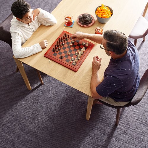 Two people playing chess at a wooden table in a room with purple carpet from Rugtex of Florida in Miami, FL